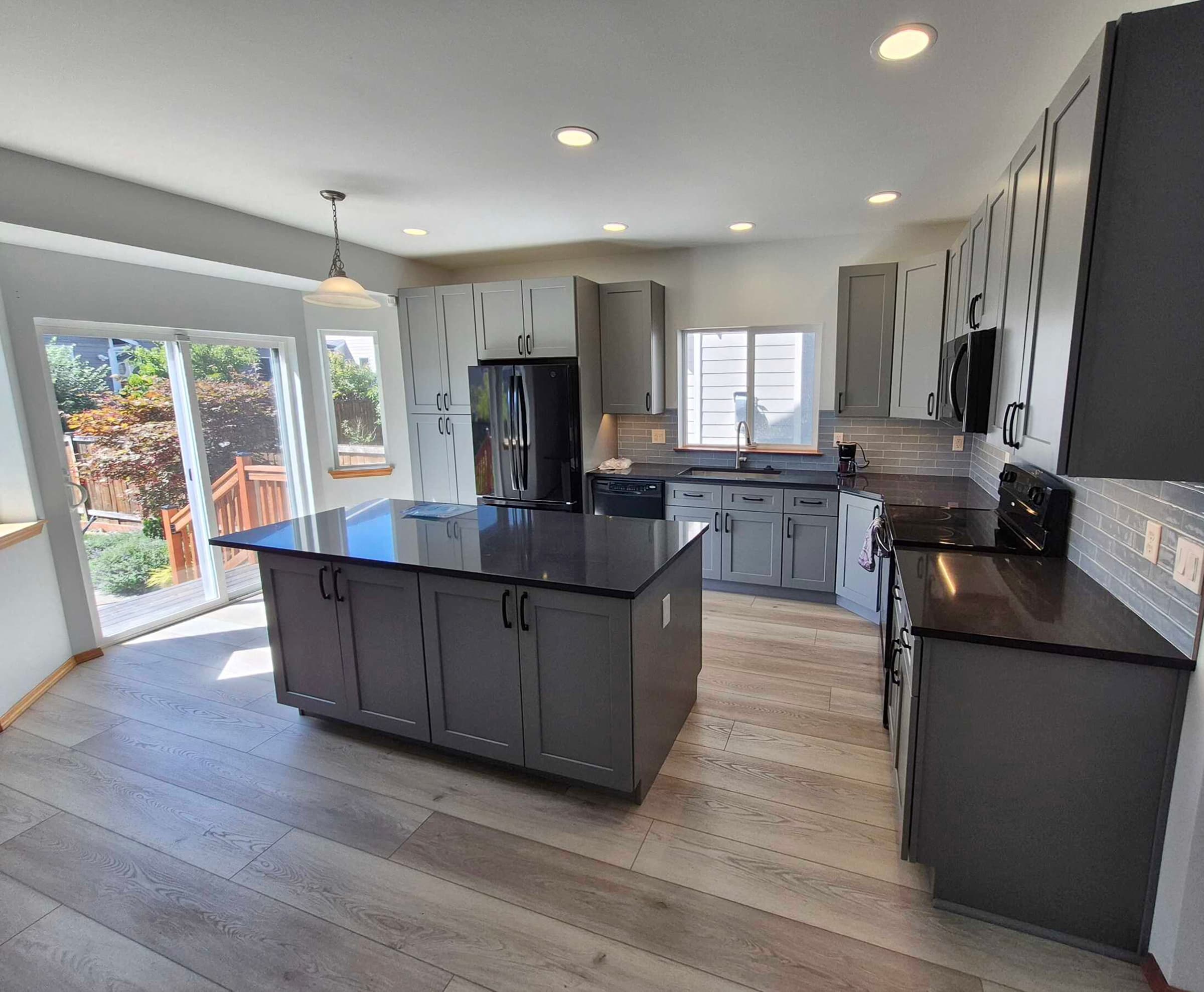 Remodeled open kitchen with a large dark-countertop island, gray shaker cabinets, and wide-plank flooring