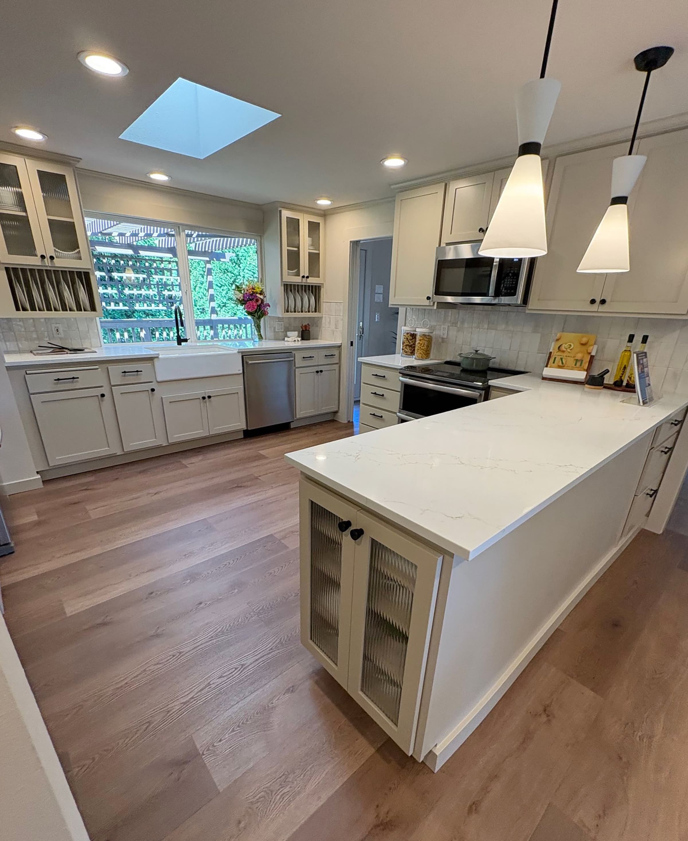 Bright remodeled kitchen with white cabinetry, quartz peninsula, farmhouse sink, and a skylight