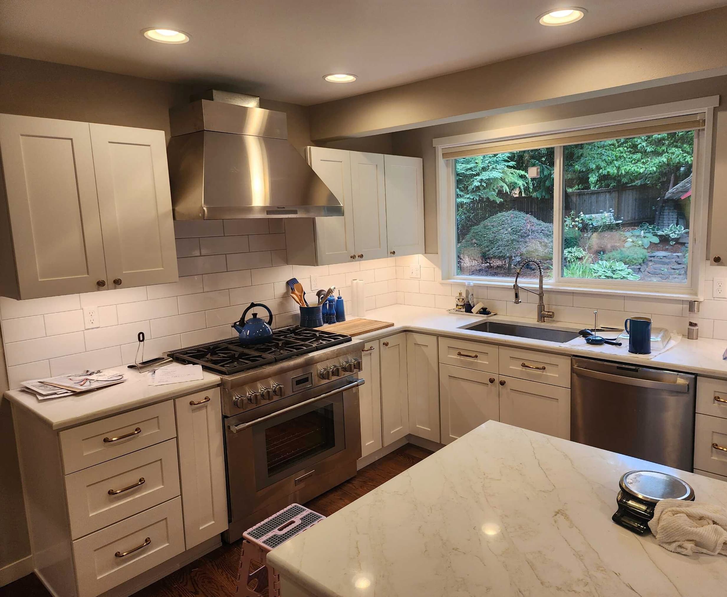 Kitchen remodel with white shaker cabinets, stainless range hood, and marble-look island