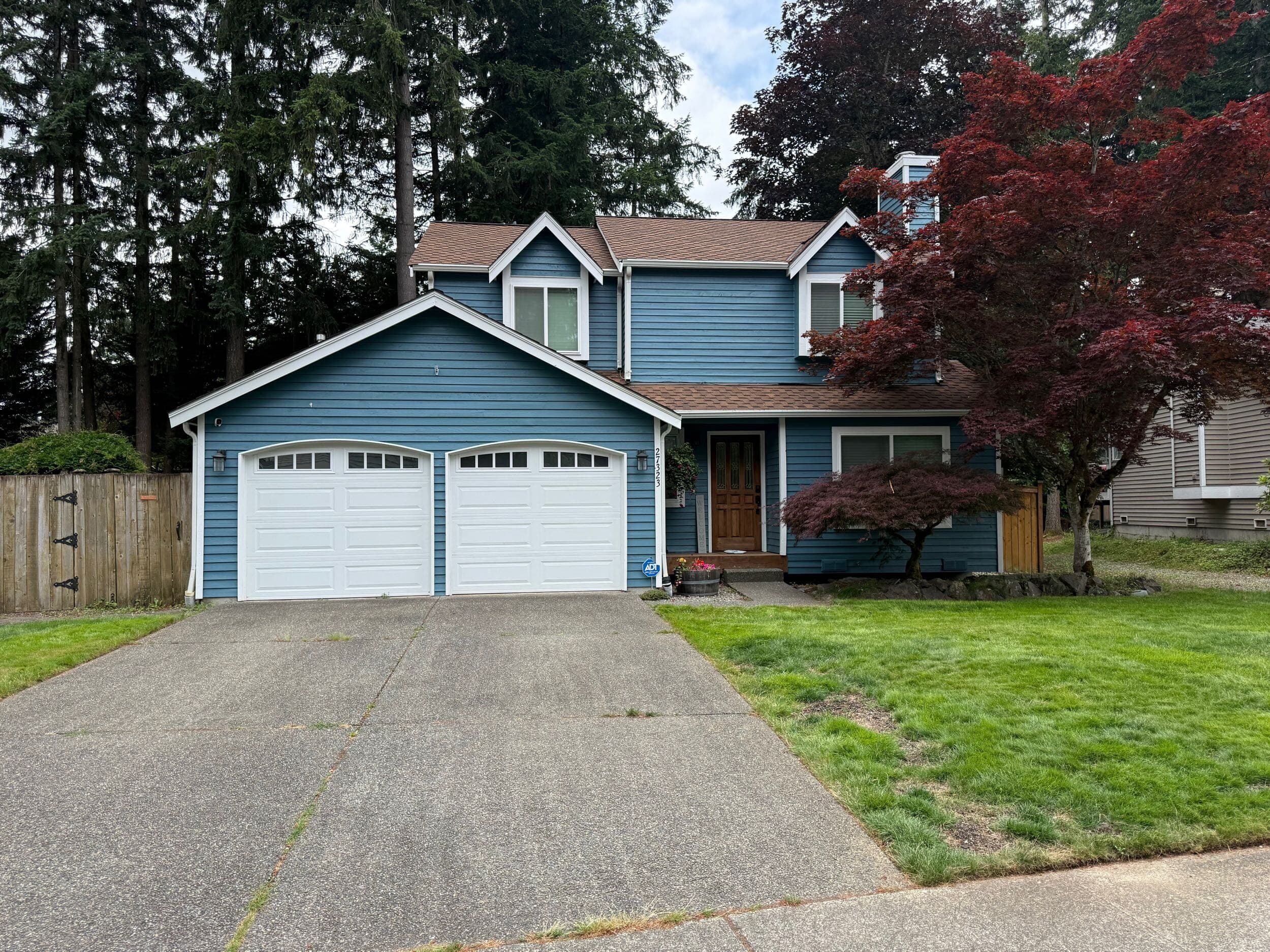 Two-story home with freshly painted blue siding, white garage doors, and landscaped yard