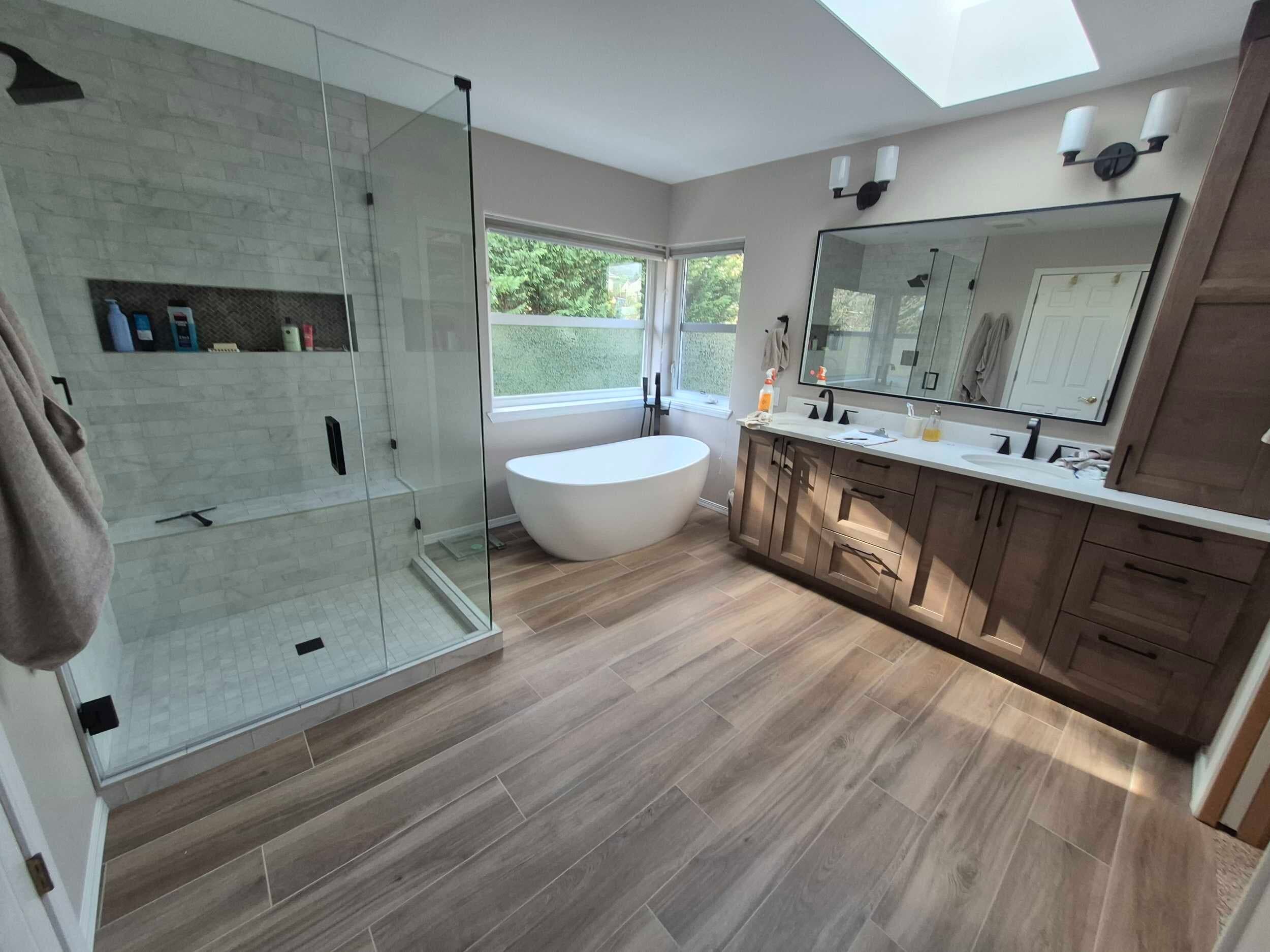 Remodeled bathroom with a glass walk-in shower, freestanding tub, double vanity, and skylight